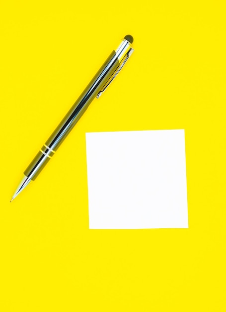 Autocollant blanc vierge de liste de tâches avec un stylo. Recherche d'informations sur Internet. Gros plan du papier de rappel sur le fond jaune. Espace de copie. Minimalisme, original et créatif.