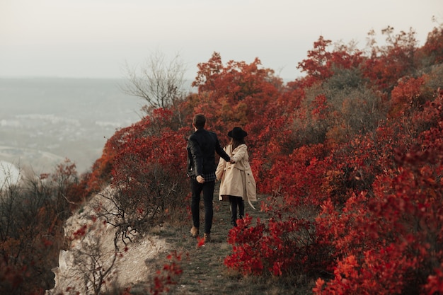 Automne beau jeune couple dans des vêtements élégants marche au sommet de la colline et se tenant la main