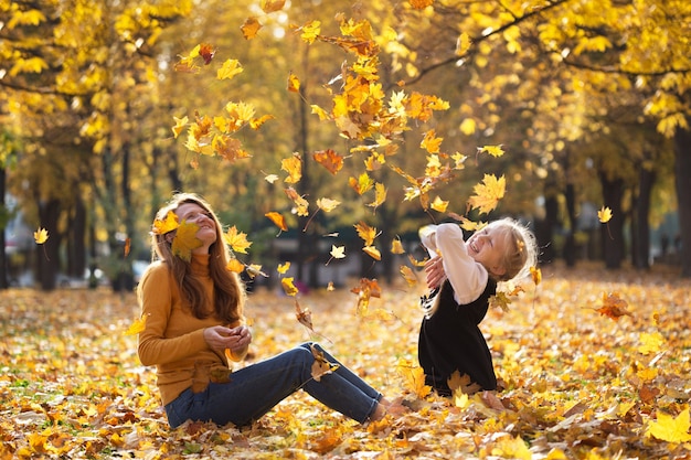 Automne. famille heureuse - mère souriante avec fille à l'extérieur jeter des feuilles d'érable jaune