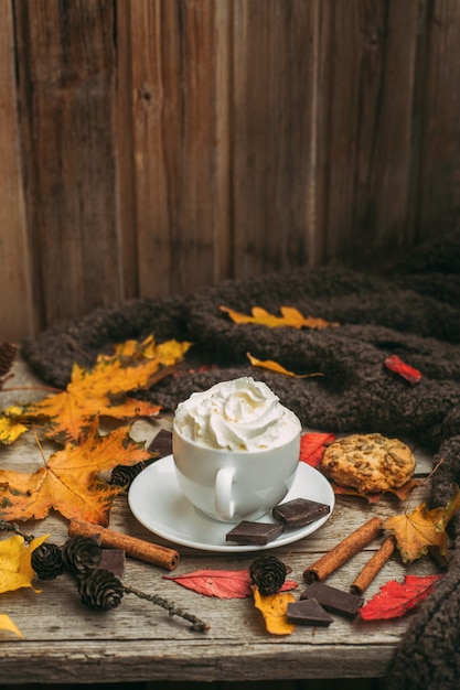 L'automne, les feuilles d'automne, une tasse de café fumant et une écharpe chaude sur une table en bois.