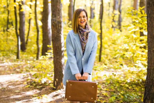 Automne, mode, concept de personnes - femme avec valise rétro marron marchant dans le parc en automne