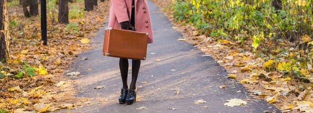 Automne, mode, concept de personnes - gros plan d'une femme avec une valise rétro marron marchant dans le parc d'automne