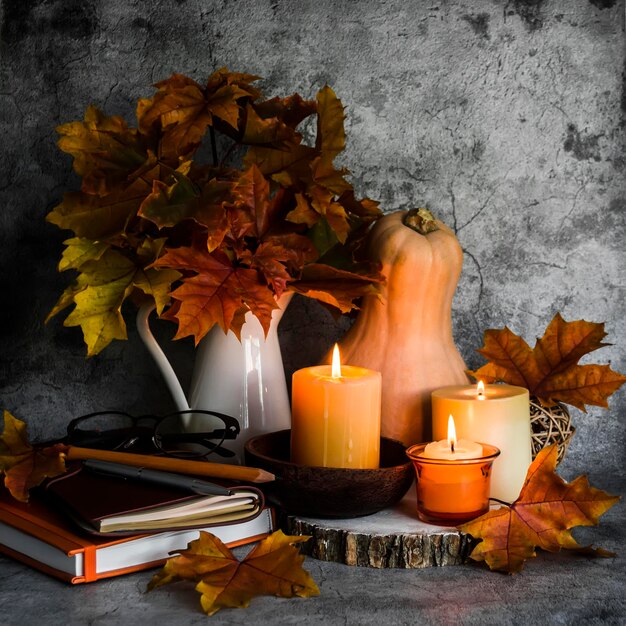 Automne nature morte bougies allumées bouquet de feuilles d'érable livres citrouille sur fond gris