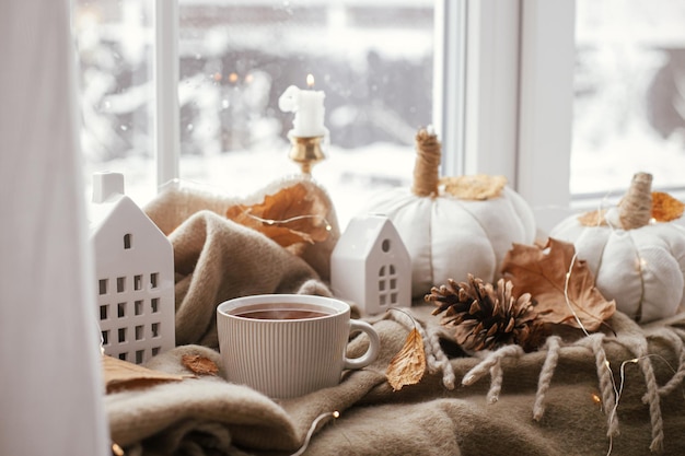 Automne nature morte tasse de thé chaude oreillers citrouilles confortables feuilles d'automne bougies et décoration de bâtiments mignons sur une écharpe marron sur le rebord de la fenêtre Hygge automne décor à la maison Happy Thanksgiving