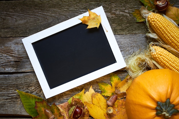 Photo automne de thanksgiving, surface en bois avec citrouilles, feuilles fanées, glands, châtaignes et un cadre pour les inscriptions