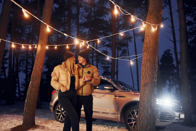 Automobile garée derrière Couple debout dans la forêt et célébrant le nouvel an