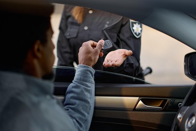 Automobiliste en gros plan donnant la clé à la policière. Conséquences d'un accident de voiture ou d'un dépassement de la limite de vitesse