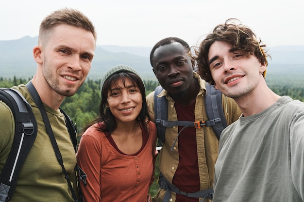 Autoportrait de jeunes randonneurs interraciaux positifs se tenant ensemble dans les montagnes pendant l'aventure