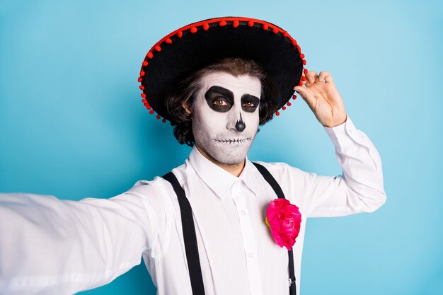 Autoportrait de son beau monsieur effrayant et effrayant portant un sombrero touchant Santa Muerte catrina thème célébration de l'événement festal isolé brillant vif éclat fond de couleur bleu vif