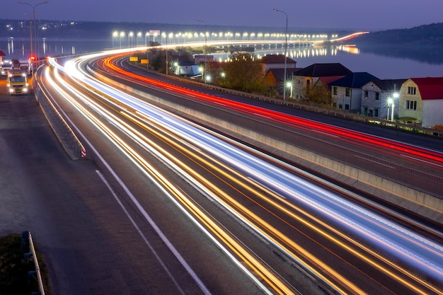 Autoroute de banlieue en fin de soirée. Traces de phares et feux arrière de circulation dense et feux sur le pont