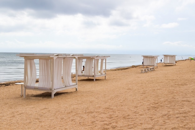 Auvents avec des rideaux blancs sur la plage de sable au bord de la mer. Nuages gris.