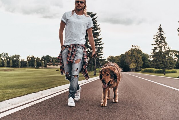 Avancer ensemble. Toute la longueur du beau jeune homme marchant avec son chien tout en passant du temps à l'extérieur