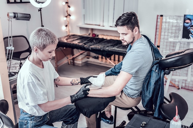 Avant de faire un tatouage. Maître de tatouage féminin professionnel pulvérisant de l'alcool sur la main nue en le séchant