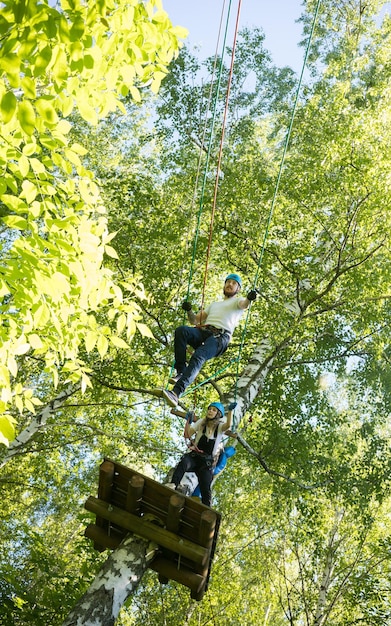 Aventure de corde femme et homme ayant un divertissement de corde dans la forêt verte debout en haut et marchant sur la corde