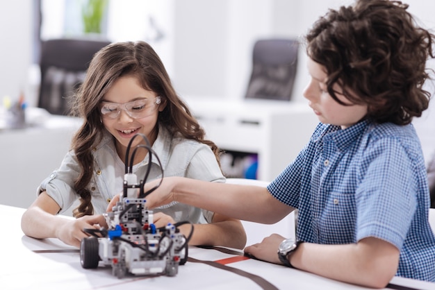 Aventure scientifique. Heureux enfants qualifiés heureux assis à l'école et créant un robot tout en exprimant la joie