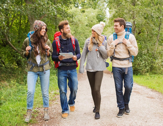 aventure, voyage, tourisme, randonnée et concept de personnes - groupe d'amis souriants avec sacs à dos et carte marchant à l'extérieur