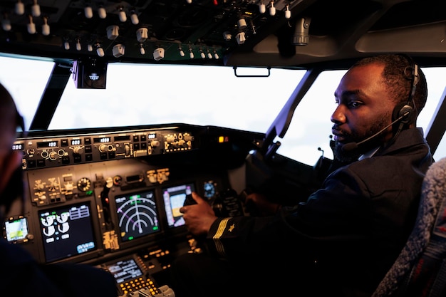 Aviateur afro-américain volant en avion en équipe avec le capitaine, utilisant la commande et la navigation du tableau de bord. Équipe d'avions de ligne poussant les boutons du panneau de commande et le levier pour décoller et voler.