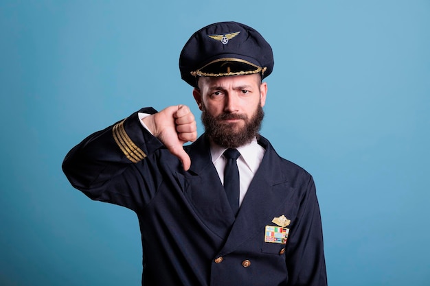 Aviateur d'avion sérieux avec le geste du pouce vers le bas portant un portrait uniforme professionnel, pilote d'avion regardant la caméra. Membre d'équipage montrant un signe de désapprobation avec les doigts, plan moyen en studio