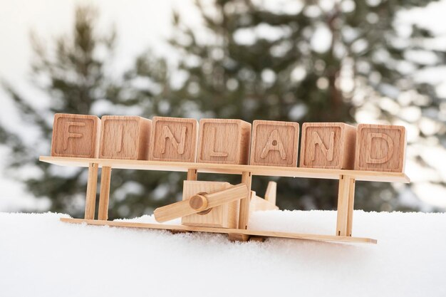 Un avion en bois et le mot Finlande fait de cubes sur le fond d'une forêt enneigée Le concept de voyager dans les pays scandinaves Carte postale dans un style rétro Vol vers la Finlande