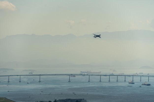 Avion décollant de la piste de l'aéroport de Rio de Janeiro Brésil Rio Niteroi Bridge montagnes et navires en arrière-plan Dawn avec un peu de brouillard