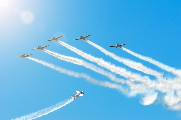 Un avion à moteur léger avec une trace de fumée blanche vole en groupes dans le ciel bleu avec la lumière du soleil et l'éblouissement.