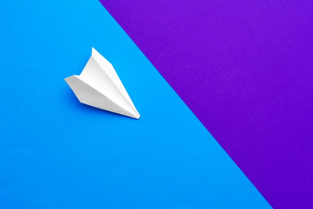 Avion en papier blanc sur un bloc de couleur bleu et violet