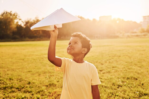 Avec un avion en papier, un enfant afro-américain s'amuse sur le terrain pendant la journée d'été