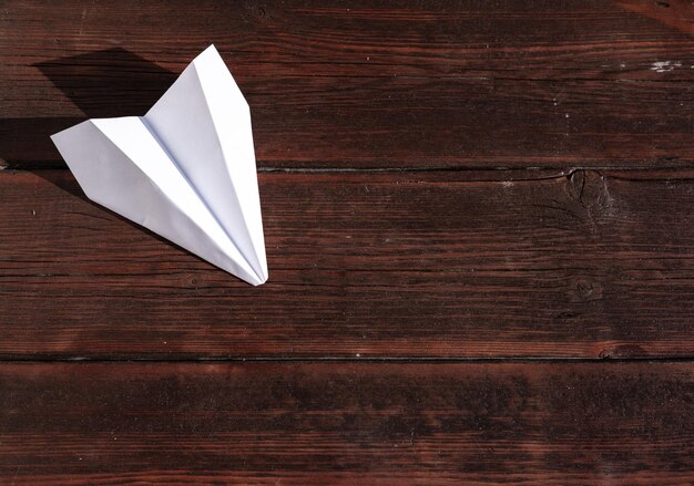 Un avion en papier est allongé sur une table en bois Avion en papier blanc sur la table