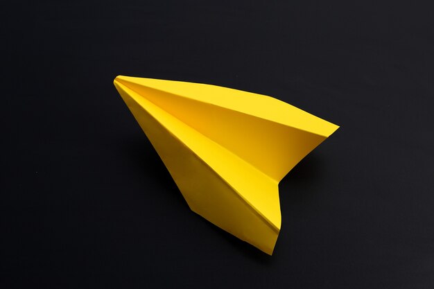 Avion en papier jaune sur une surface sombre.