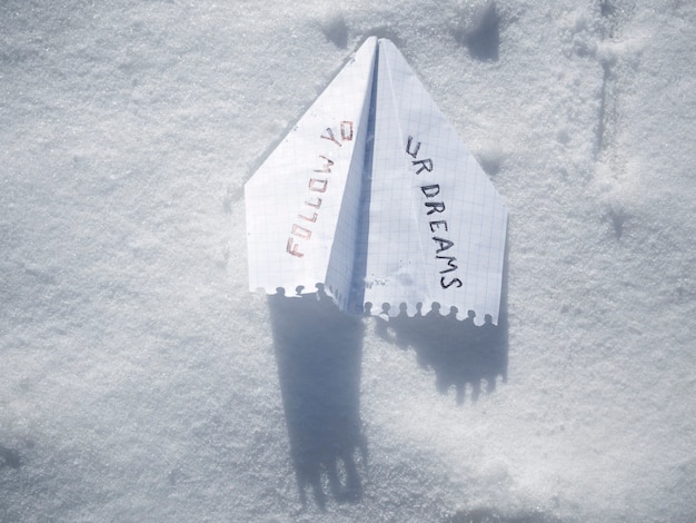 Avion en papier sur neige blanche avec phrase suivez vos rêves