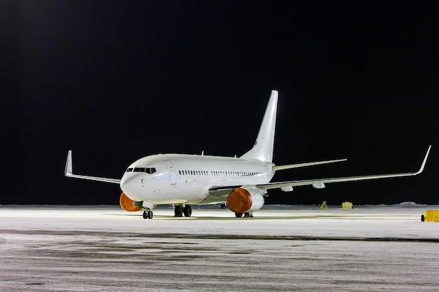 Avion de passagers blanc sur le tablier de l'aéroport de nuit en hiver