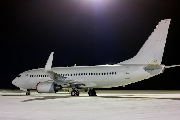 Avion de passagers blanc sur le tablier de l'aéroport de nuit en hiver