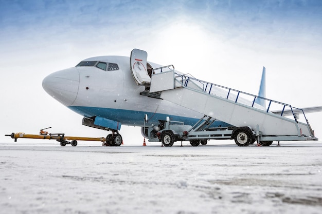 Avion de passagers avec un escalier d'embarquement sur le tablier de l'aéroport dans une tempête de neige