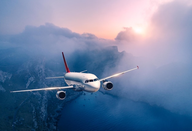 Photo avion de passagers survole les nuages au coucher du soleil paysage avec avion blanc nuages bas côte de la mer ciel violet au crépuscule l'avion atterrit voyage d'affaires avion commercial voyage vue aérienne