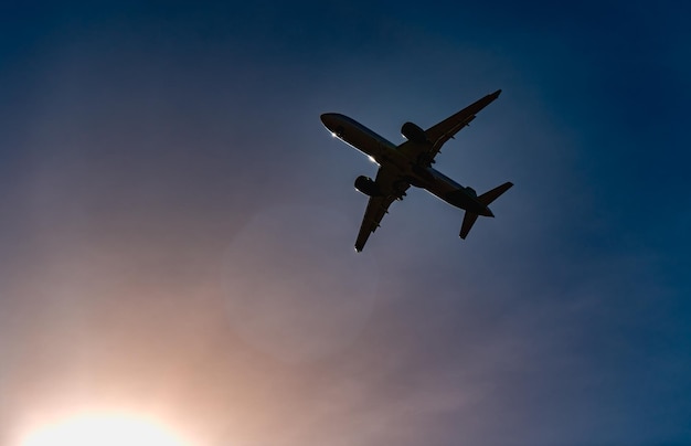 Avion de passagers Voir exactement d'en bas la silhouette contre le ciel bleu et le coucher du soleil