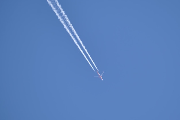 Avion à réaction de passagers lointain volant à haute altitude sur un ciel bleu clair laissant une trace de fumée blanche de traînée derrière. Notion de transport aérien.