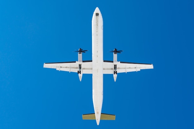 Avion à turbopropulseur avec moteurs à hélices sur les ailes avant d'atterrir sur une piste à l'aéroport contre un ciel bleu.