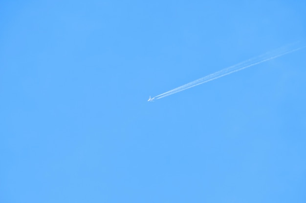 Avion volant avec une traînée blanche dans le ciel bleu. Fond minimal.