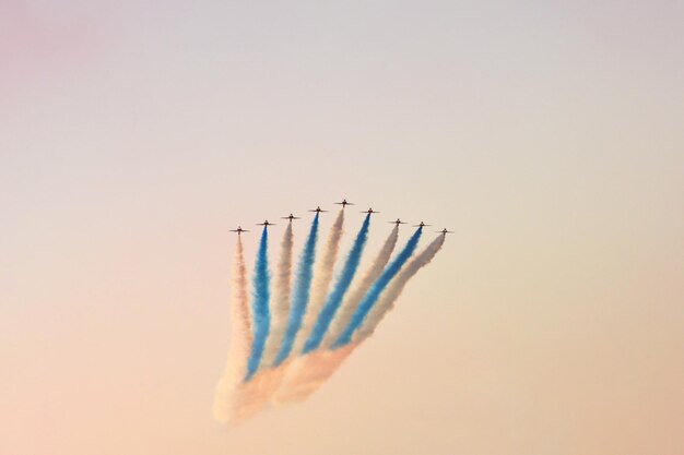 Des avions de chasse militaires volent en groupe avec de la fumée dans le ciel bleu