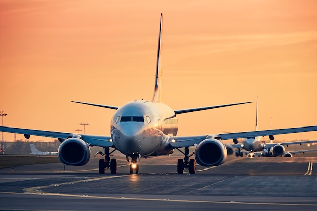 Des avions en rangée se dirigeant vers la piste de décollage pour le trafic à l'aérodrome occupé au coucher du soleil