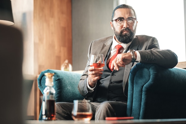 Avocat buvant. Avocat aux cheveux noirs barbu, boire de l'alcool et fumer un cigare assis dans un fauteuil confortable