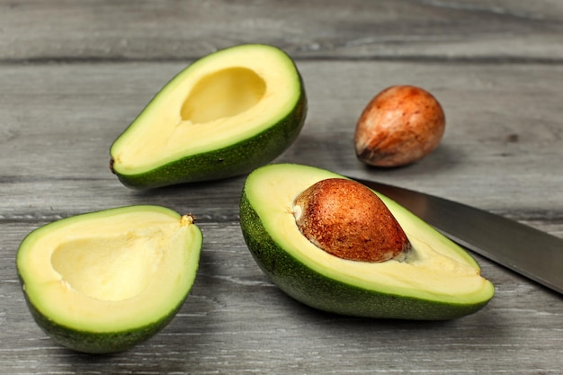 Avocat, coupé en deux, deux graines et couteau de chef sur un bureau en bois gris.