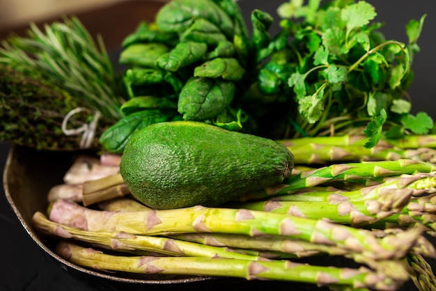 Avocat et divers légumes verts sur fond sombre Asperges épinards romarin Concept de cuisine végétarienne