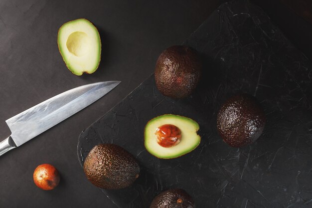 Avocat Hass bio tranché et entier avec un couteau sur une surface noire