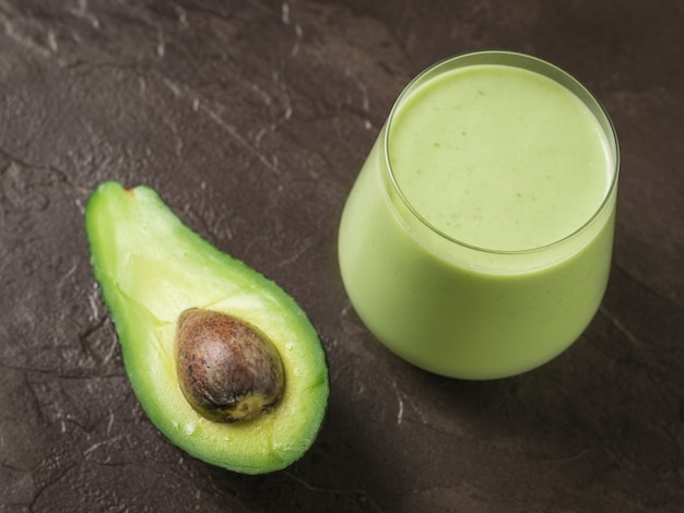 Avocat et un verre de smoothies aux épinards et à l'avocat sur fond de pierre. Produit de remise en forme. Nutrition sportive diététique.