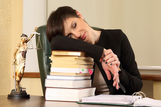 Avocate fatiguée au bureau avec des livres et des documents