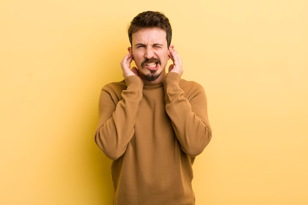 Avoir l'air en colère, stressé et agacé, couvrant les deux oreilles d'un bruit assourdissant ou d'une musique forte