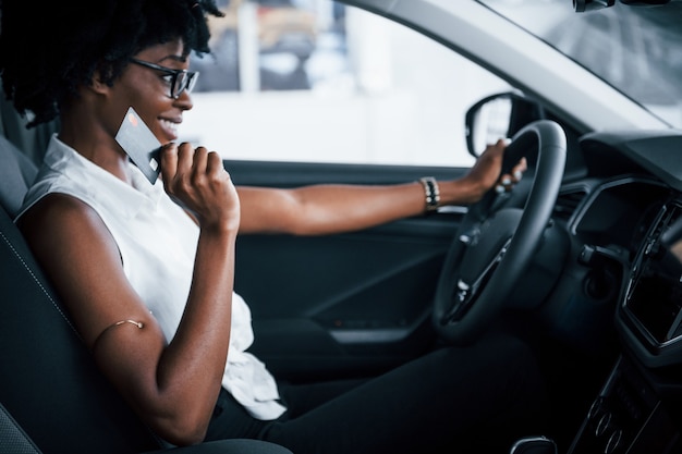 Avoir un appel. Une jeune femme afro-américaine est assise à l'intérieur d'une nouvelle voiture moderne.