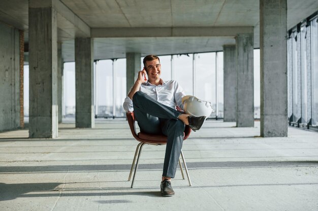 Avoir une conversation en utilisant le téléphone Jeune homme en tenue de soirée travaille à l'intérieur sur la construction