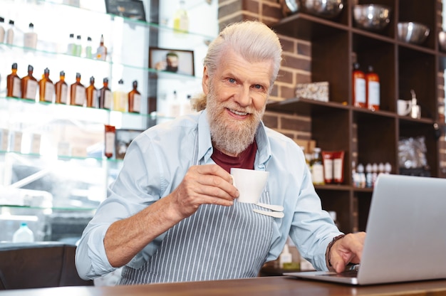 Avoir une pause. Joyeux homme barbu tenant la tasse dans la main droite, regardant directement la caméra